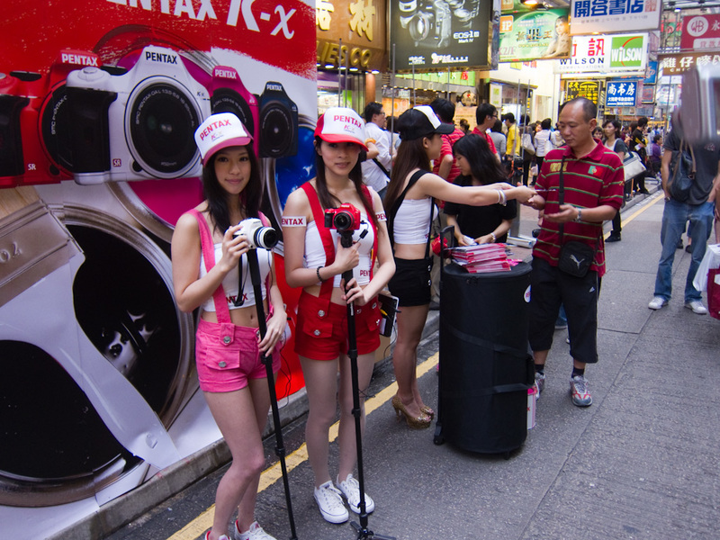 Hong Kong-Mong Kok - Heres some girls advertising pentax cameras being photographed by lots of people with non pentax cameras.