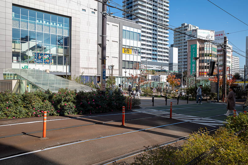 Japan-Tokyo-Walking-Yamanote - Station 9 of 30 - Otsuka. Hard to read the sign. A tram runs in front of the station.